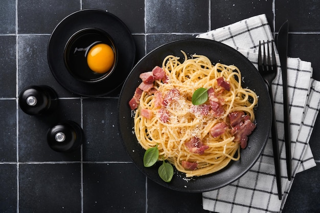 Carbonara pasta Spaghetti with pancetta egg parmesan cheese and cream sauce on old black tile table background Traditional italian cuisine and dish Pasta alla carbonara Top view