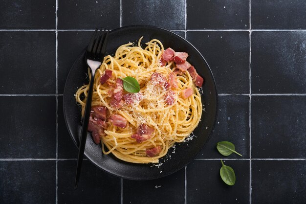 Pasta alla carbonara spaghetti con pancetta uovo parmigiano e salsa di panna su sfondo vecchio tavolo piastrellato nero cucina tradizionale italiana e piatto pasta alla carbonara vista dall'alto