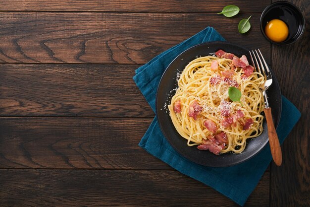 Carbonara pasta Spaghetti with pancetta egg parmesan cheese and cream sauce on old dark black wooden table background Traditional italian cuisine and dish Pasta alla carbonara Top view