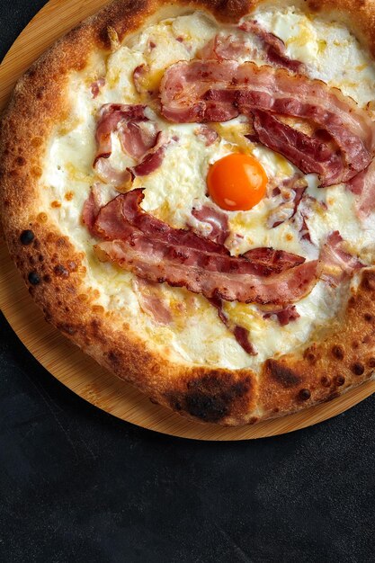 Carbonara pizza with bacon and egg on dark stone background