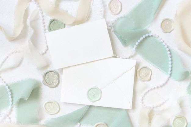 Card and envelope near light green and beige decor and silk ribbons on white table top view mockup