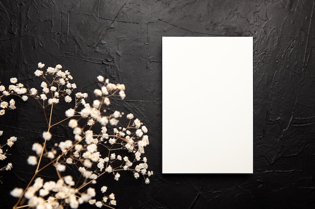 검은색 배경에 흰색 꽃 장식이 있는 카드 모형 빈 청첩장 테이블에 말린 꽃이 있는 인사말 카드 모형