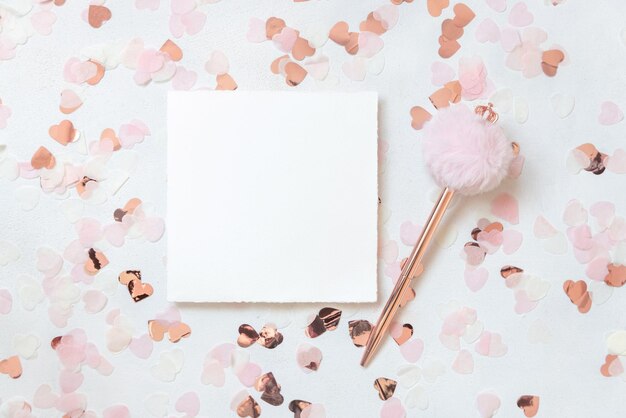Photo card and pen between pink hearts on white table top view valentines mockup