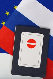 Carta con un segno di divieto di accesso posto su un passaporto di servizio di un funzionario internazionale. sullo sfondo due bandiere dell'ue e della russia. vista dall'alto. spazio libero per un testo