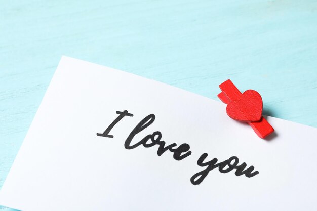 Card with text I Love You and red clothespin on light blue wooden background closeup