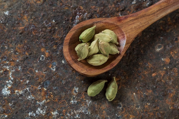 Cardamom pods in wooden spoon on a textured