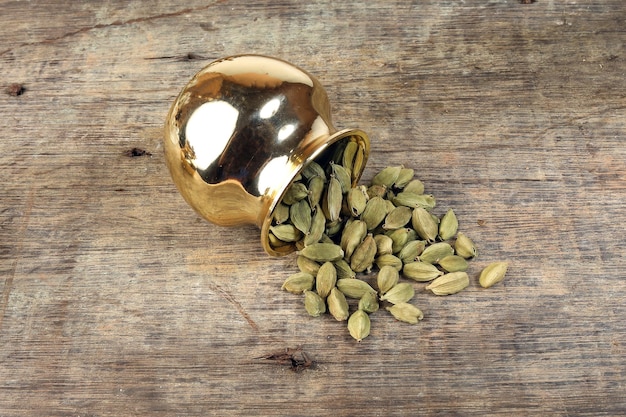 Cardamom spice in golden metal pot on rustic wood