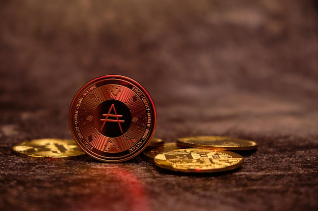 Cardano cryptovaluta ADA goud met een onscherpe achtergrond met roodachtige tinten zoals vuur