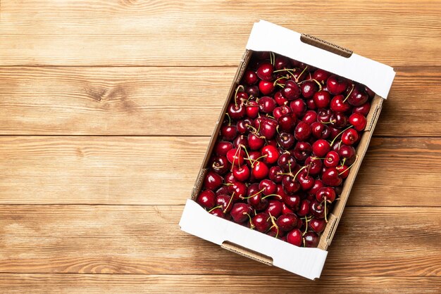 Картонная коробка с красными вишнями на деревянном столе Продажа вишни Здоровые ягоды
