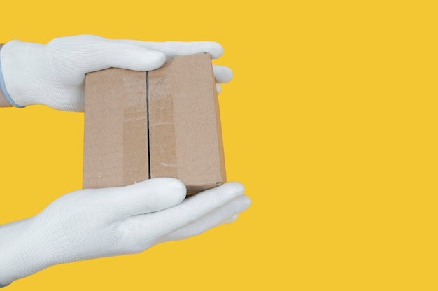 Photo a cardboard box in the hands of white gloves on a yellow background