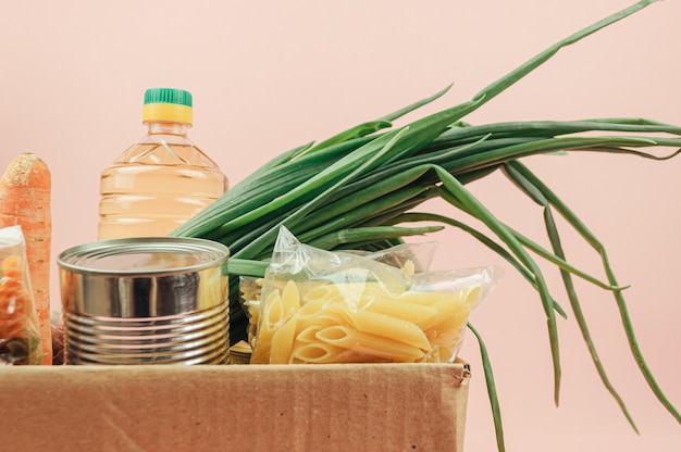 Cardboard box isolated on a pink background with butter, canned\
goods, onions, cookies, pasta, fruits. food delivery.