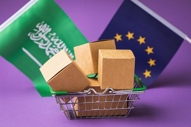 Cardboard boxes in a food basket and flags the concept of trade between the EU and Saudi Arabia