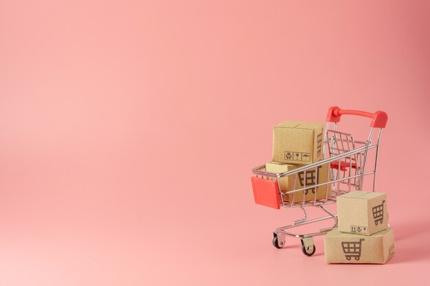 Cardboard boxes in red shopping cart on pink background.