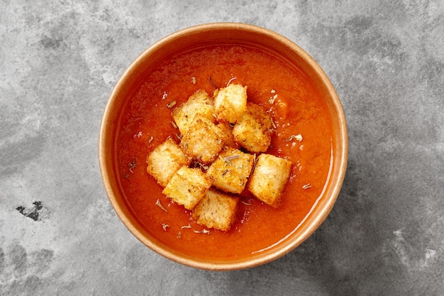 Cardboard cup of refreshing tomato soup gazpacho with croutons and dried herbs on gray background