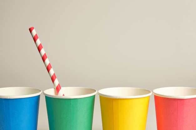 Photo cardboard cups of blue yellow green and red placed in line on a gray background with side light with a red and white straw inside the green