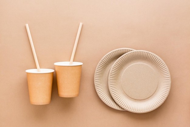 Cardboard cups drinking straws and plates on a beige background Eco friendly and zero waste concept Top view