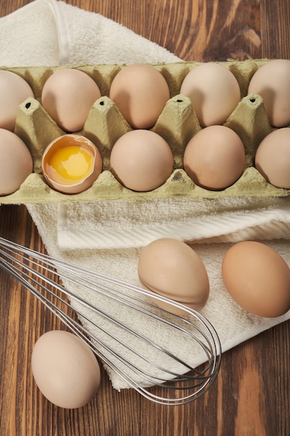 Cardboard egg box and egg beater on wooden table. Top view