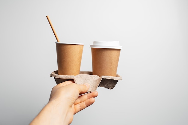 Cardboard holder with two paper cups of coffee takeaway in male hand on white