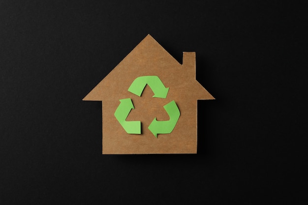 Cardboard house with recycling sign on black background, space for text