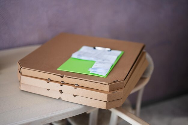 Cardboard pizza boxes with delivery clipboard on kitchen in table