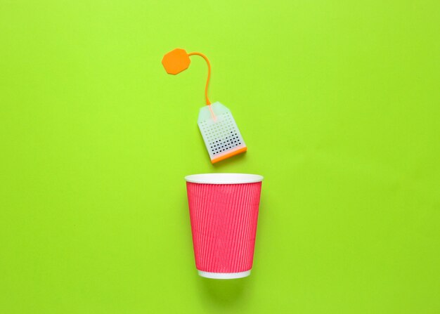 Cardboard tea cup and teabag on green background