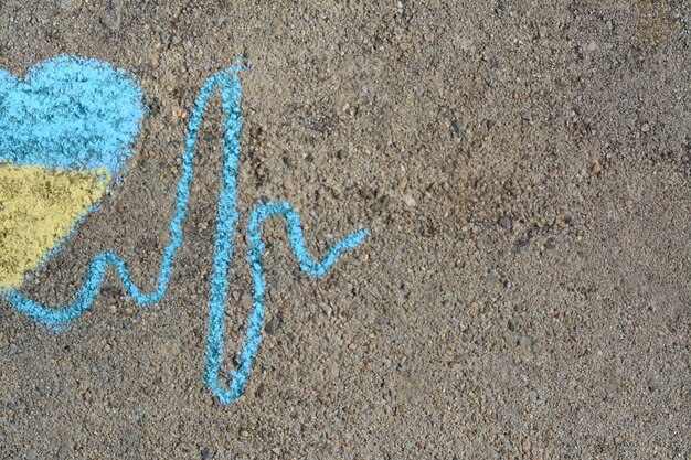 Cardiogram line with heart drawn by blue and yellow chalk on asphalt top view Space for text