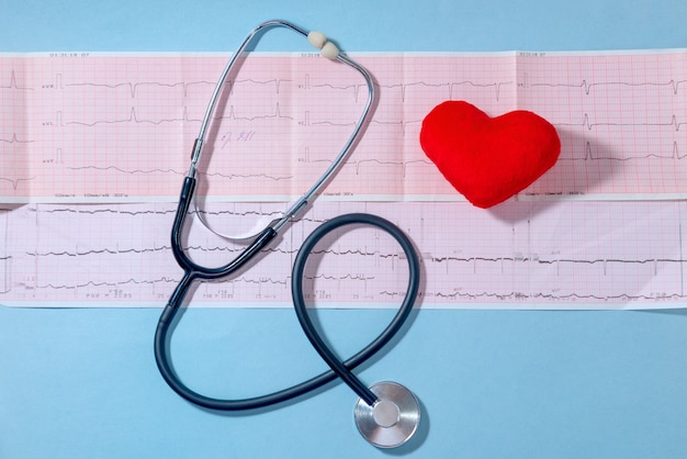 Cardiogram with Medical stethoscope and red heart on a blue table, close up