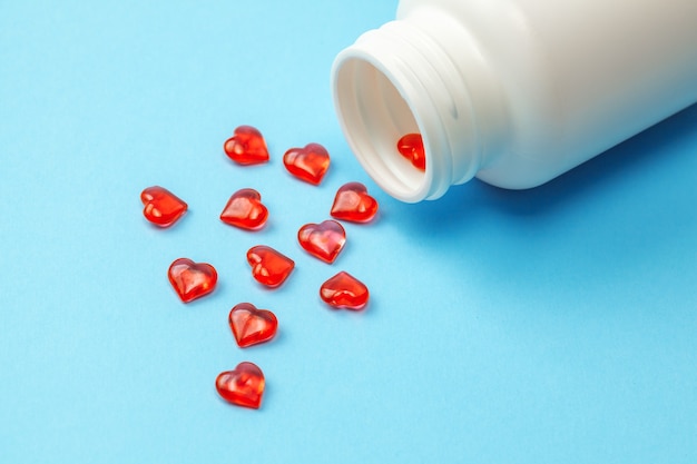 Cardiology pills. Red pills in the shape of heart with bottle on blue background.