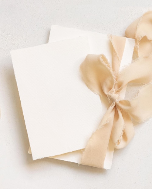 Photo cards tied with a beige silk ribbon on white table top view copy space wedding stationery mockup