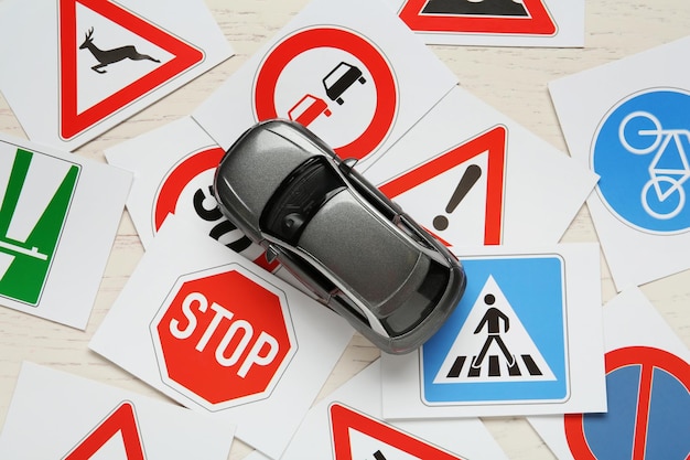 Cards with different road signs and toy car on white wooden table flat lay Driving school