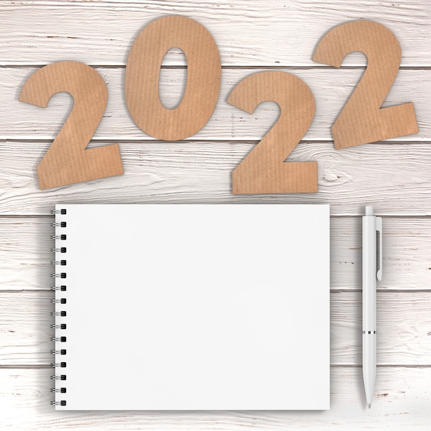 Foto cardstock numbers 2022 happy new year sign in de buurt van white spiral paper cover notebook met pen over houten tafel achtergrond. 3d-rendering