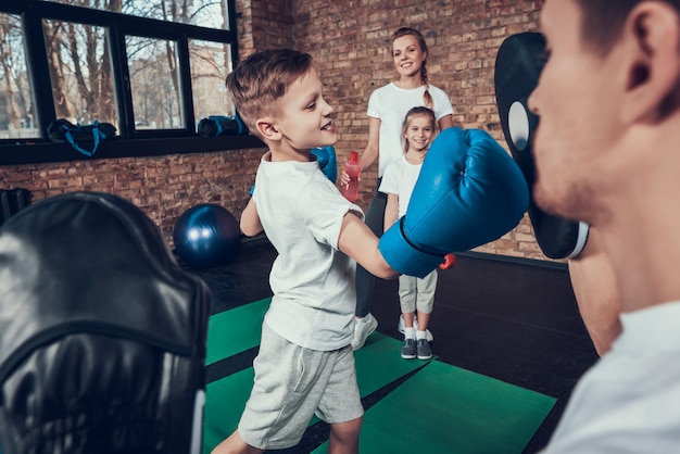 Care father trains little boxer in gloves in gym.