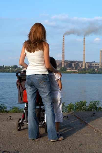 "care future" concept. Young mother with her kids are looking at the chimney-stalks polluting an air