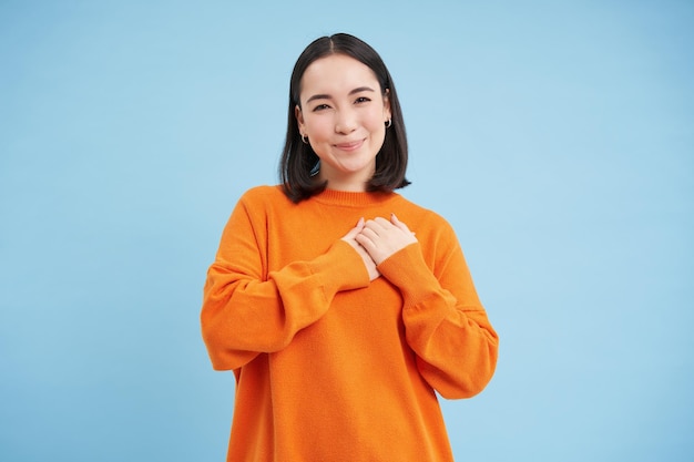 Care and love asian woman holds hands on heart and smiles looks with tenderness and warmth at camera
