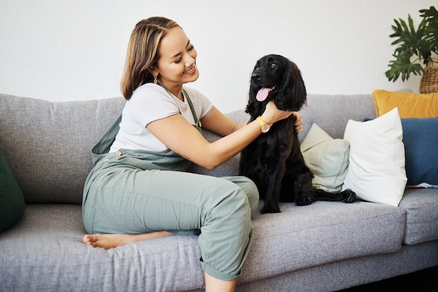 家のソファでリラックスして動物と遊ぶ愛と犬を飼う女性ペットの飼い主が床にいて、仲間の笑顔と健康や友情を持って、居心地の良いアパートで一緒に幸せなアジア人