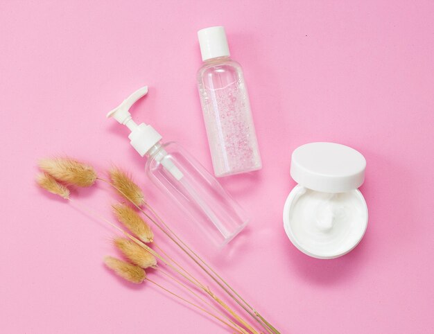 Cura, cosmetici biologici per il viso. bottiglie bianco crema e trasparenti su fondo rosa