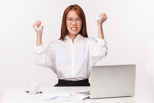 Career, work and women entrepreneurs concept. Close-up portrait of pissed-off bothered asian office lady, manager hate paperwork, squeeze documents from anger and annoyance, sit near laptop