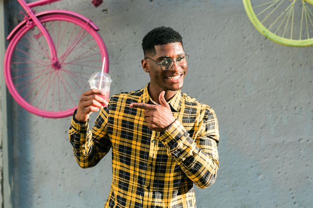 Carefree african american guy in casual wear holding tropical cocktail urban summer background cool
