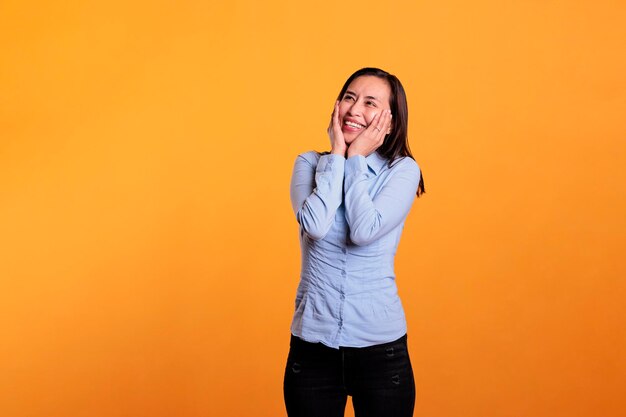 Carefree asian woman smiling in front of camera, posing with joyful expressions over in studio yellow background. confident cheerful young adult feeling excited and happy enjoying good times