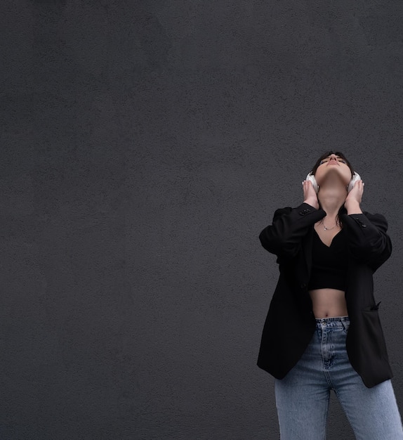 Carefree attractive brunette girl dressed in gray sweater listening to music on headphones standin