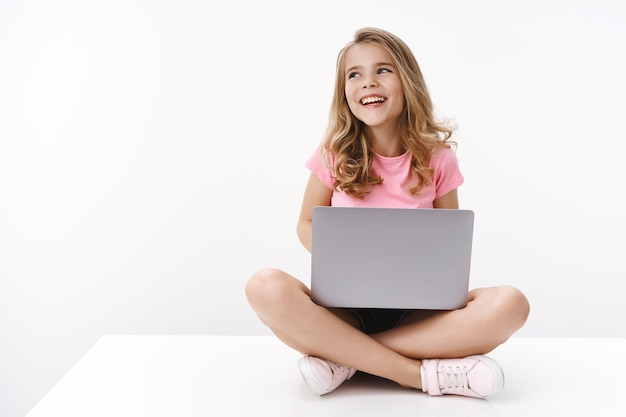 Carefree cheerful blond caucasian cute kid young sister sitting floor with laptop, laughing joyfully, studying online, digital education, look away left copyspace, smiling happy, learn new language