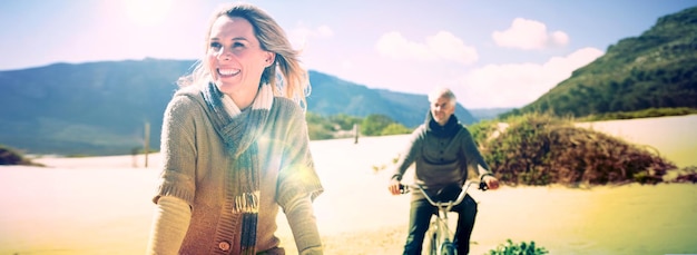 Carefree couple going on a bike ride on the beach on a bright\
but cool day