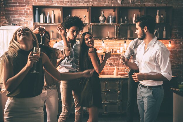 Carefree dance with friends. Cheerful young people dancing and drinking while enjoying home party on the kitchen