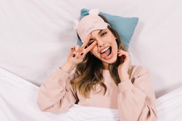 Carefree darkhaired girl chilling in bed Cute white woman in sleep mask making funny faces