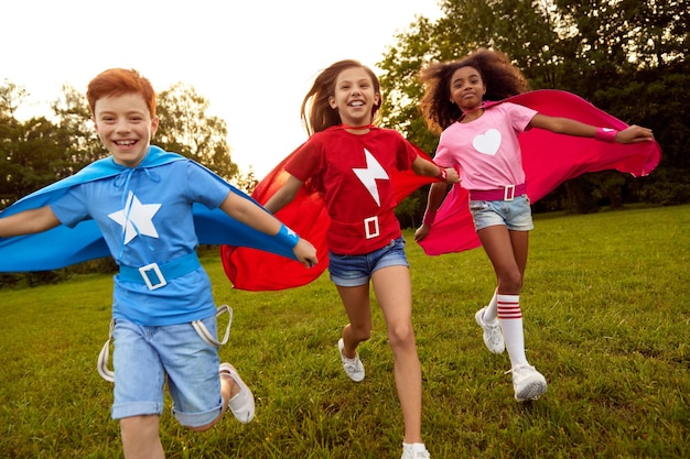 Foto bambini spensierati di supereroi diversi che corrono lungo il prato