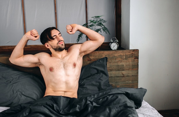 Carefree guy enjoying new day. Sexy, happy bearded man in bed