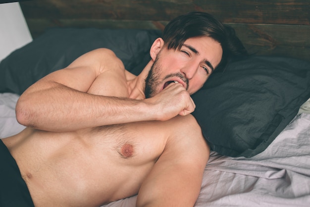 Carefree guy enjoying new day. Sexy, happy bearded man in bed