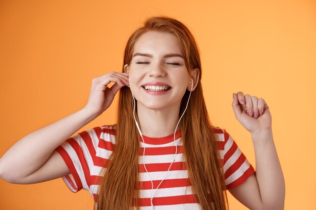 Carefree happy redhead woman put earphone smiling delighted listen favorite song close eyes relaxed ...