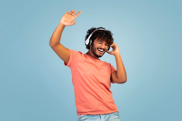 Carefree indian guy listening to music and dancing using
headphones