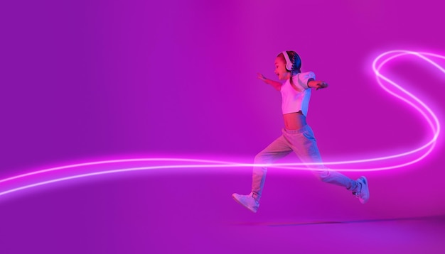 Carefree little girl with wireless headphones running towards copy space